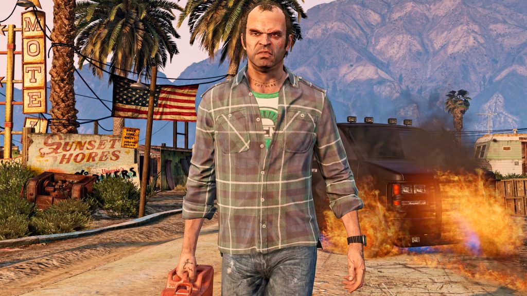 A bearded man in a stained white T-shirt standing in front of a trailer in a dusty desert town