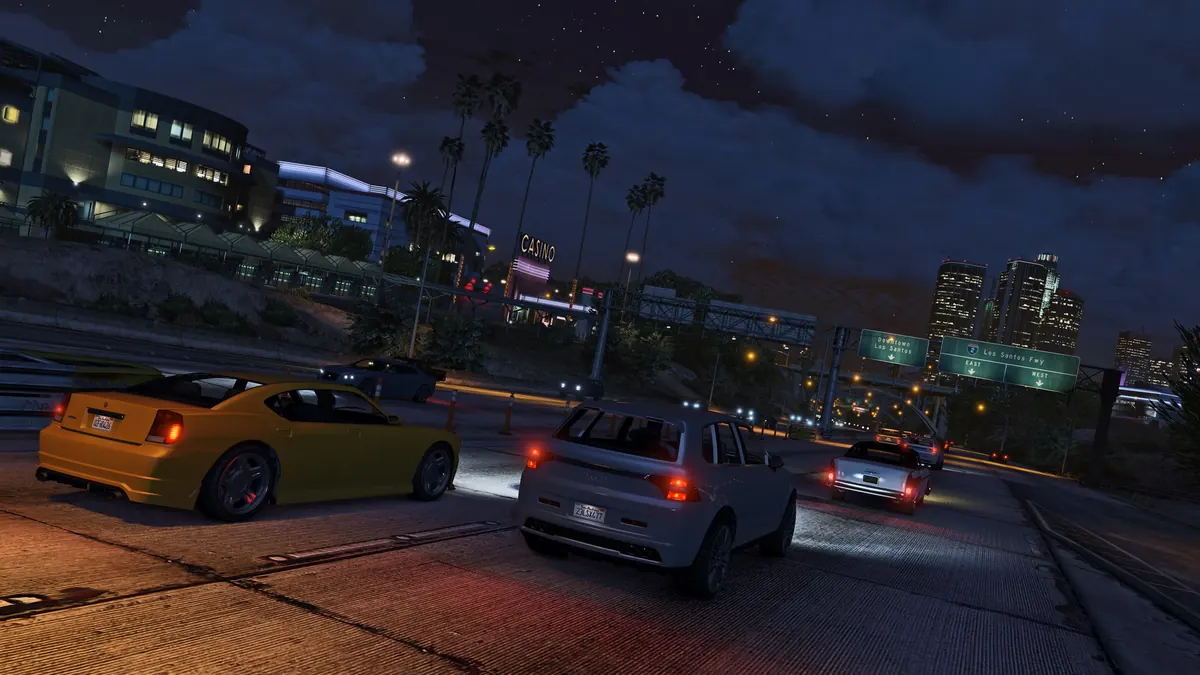 Cars driving through downtown Los Santos at night under city lights in GTA V